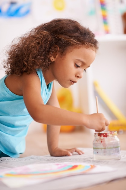 Éducation école ou fille peignant un arc-en-ciel sur le sol de la salle de classe pour l'apprentissage créatif ou le développement de l'enfant éclaboussure de couleur de papier ou enfant heureux avec l'art de la maternelle peinture croquis ou s'amuser dessin