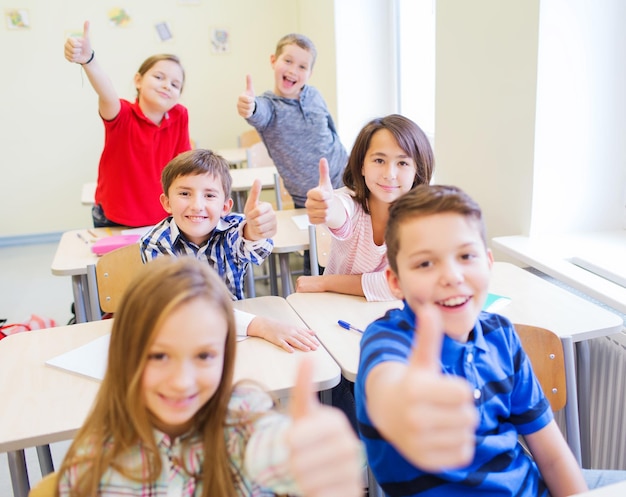 éducation, école primaire, apprentissage, concept de geste et de personnes - groupe d'écoliers assis en classe et montrant les pouces vers le haut