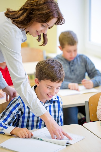 éducation, école primaire, apprentissage et concept humain - enseignant aidant un écolier à écrire un test en classe