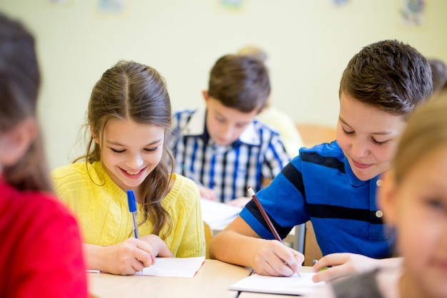 éducation, école primaire, apprentissage et concept humain - groupe d'écoliers avec test d'écriture de stylos et de cahiers en classe