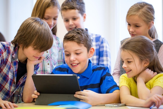 éducation, école primaire, apprentissage, technologie et concept humain - groupe d'écoliers avec ordinateur tablette s'amusant en pause en classe