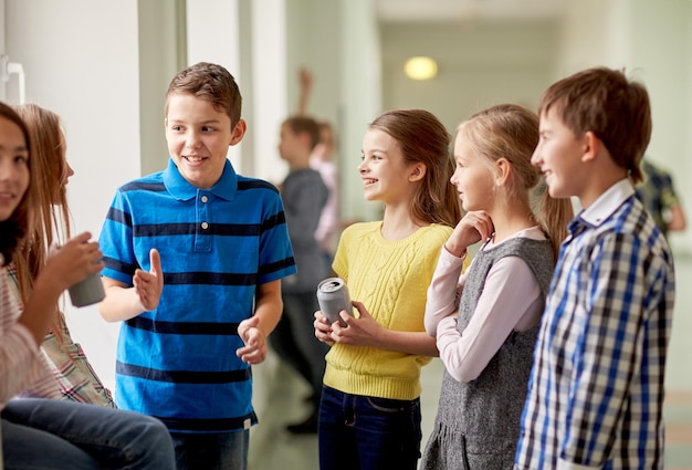 éducation, école primaire, boissons, concept d'enfants et de personnes - groupe d'écoliers avec des canettes de soda parlant dans le couloir