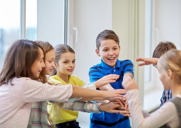 éducation, école primaire, enfants, concept de pause et de personnes - groupe d'écoliers souriants mettant les mains sur le dessus dans le couloir