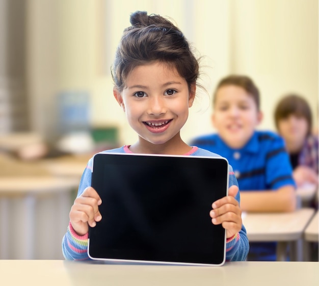 éducation, école primaire, technologie, publicité et concept d'enfants - petite étudiante montrant un écran d'ordinateur pc tablette noir vierge sur fond de classe et de camarades de classe