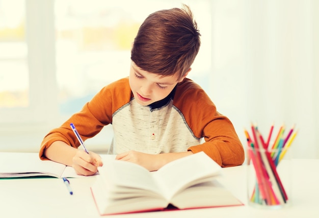 éducation, enfance, personnes, devoirs et concept d'école - étudiant garçon avec livre écrivant sur un cahier à la maison