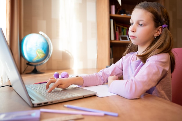 Photo Éducation en ligne des enfants une écolière enseigne une leçon en ligne à l'aide d'une conférence téléphonique par chat vidéo sur ordinateur portable avec un enseignant à la maison participant à une conférence en ligne assis au bureau