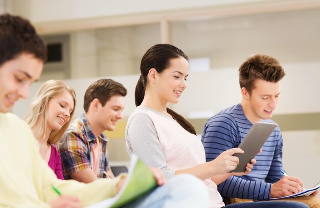 éducation, lycée, travail d'équipe et concept de personnes - groupe d'étudiants souriants avec ordinateur tablette et cahiers assis dans la salle de conférence