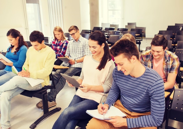 éducation, lycée, travail d'équipe et concept de personnes - groupe d'étudiants souriants avec des ordinateurs tablettes assis dans la salle de conférence