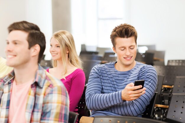 éducation, lycée, travail d'équipe et concept de personnes - groupe d'étudiants souriants avec smartphone dans la salle de conférence