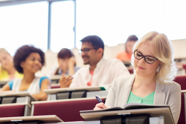 éducation, lycée, université, apprentissage et concept de personnes - étudiante écrivant sur un cahier dans une salle de conférence