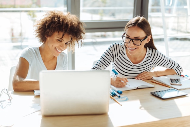 L'éducation moderne. Des étudiantes enthousiastes positives qui étudient et sont assises à la table alors qu'elles étaient assises à la table de la cafétéria