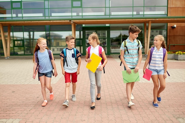 éducation primaire, amitié, enfance, communication et concept de personnes - groupe d'élèves du primaire heureux avec des sacs à dos marchant et parlant à l'extérieur