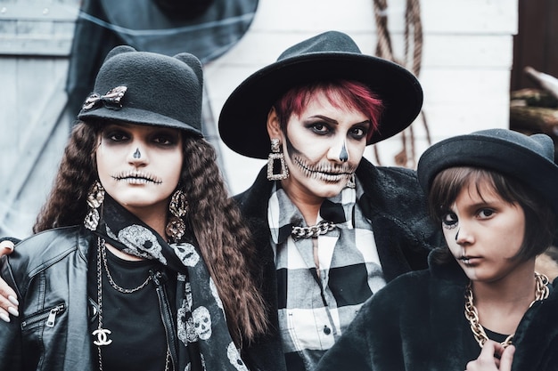 Effrayant famille mère filles célébrant halloween Terrifiant noir blanc crâne demi-visage maquillage et costumes de sorcière images élégantes Horrorfun à la fête des enfants dans la grange sur streetHatsjackets