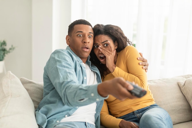 Effrayé choqué jeune femme et homme afro-américain avec canal de commutation de télécommande à la télévision regarder un film d'horreur