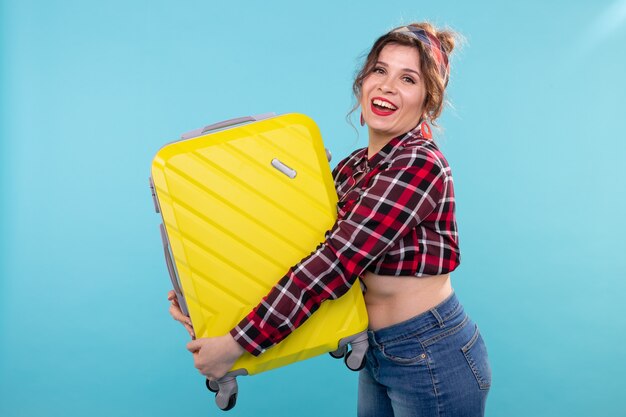 Effrayé jeune belle femme en vêtements vintage tenant une valise jaune dans ses mains posant sur