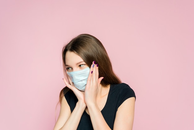 Effrayé de jeune femme dans un masque de protection sur fond rose. Peur et horreur de la pandémie de coronavirus