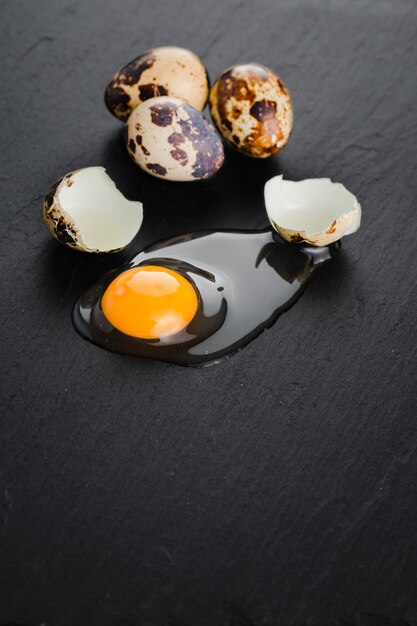 eggsufs de caille sur fond de pierre noire, œuf de caille cassé et fêlé, jaune d'œuf de caille. Produit biologique.