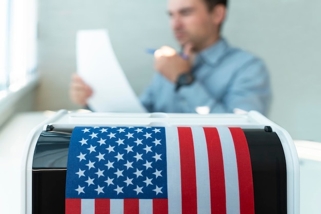 L'électeur masculin vote dans un bureau de vote L'urne est au premier plan avec un drapeau américain