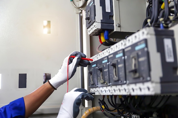 L'électricien contrôle à la main et au voltmètre la tension du courant électrique au disjoncteur
