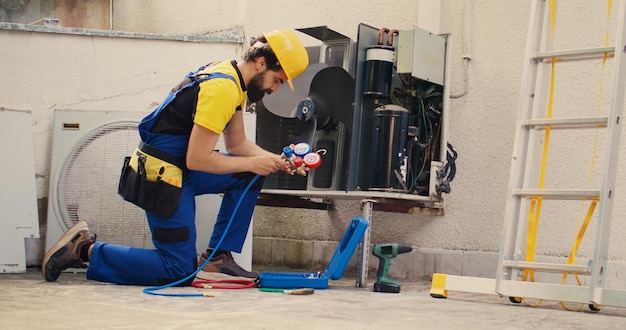 Photo Électricien effectuant une enquête annuelle sur le système hvac, assemblant des jauges de collecteur avant de le monter sur le condenseur.