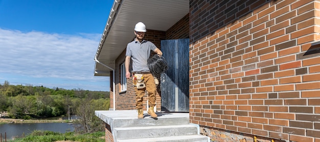 Un électricien examine un chantier de construction tout en tenant un câble électrique à la main sur le chantier.