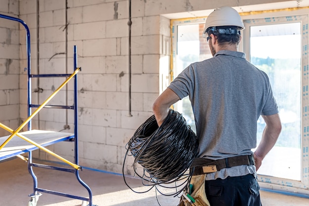 Un électricien Examine Un Dessin De Construction Tout En Tenant Un Câble électrique à La Main Sur Un Chantier.