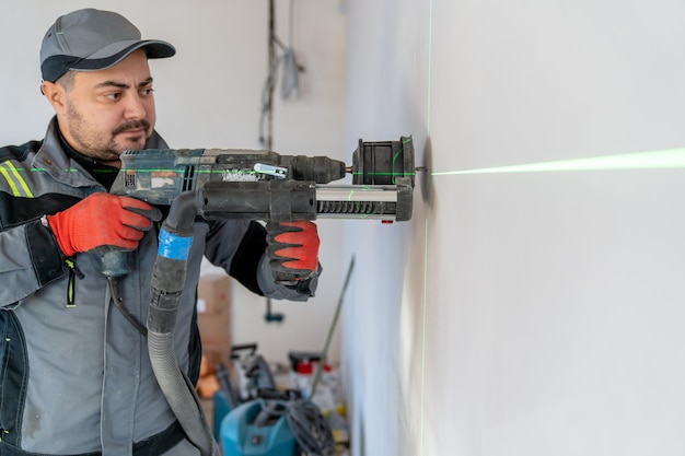 Un électricien fait un évidement dans le mur pour une prise en place marquée d'un pointeur laser