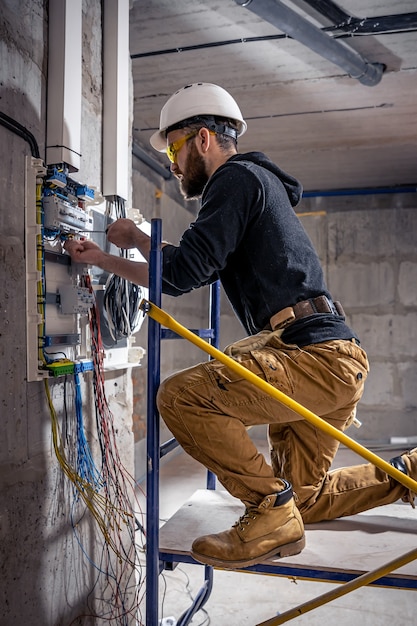 Un électricien de sexe masculin travaille dans un standard avec un câble de raccordement électrique.