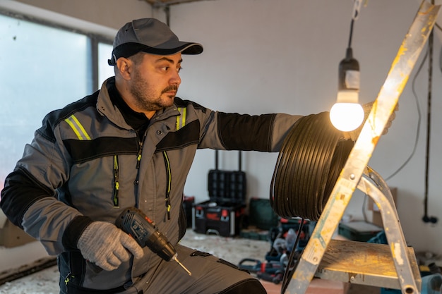 Un électricien avec un tournevis et une bobine de fil veut grimper sur une échelle