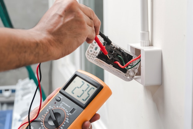 Photo l’électricien utilise un compteur numérique pour mesurer la tension à la prise de courant