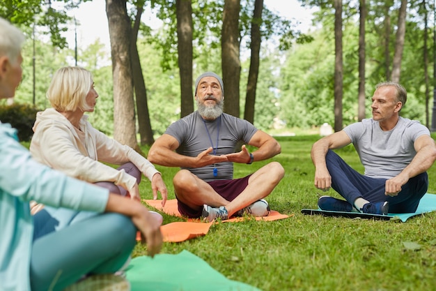 Élégant Entraîneur De Yoga Barbu Assis Sur Un Tapis Démontrant à Ses Clients Seniors Comment Faire De L'exercice Respiratoire