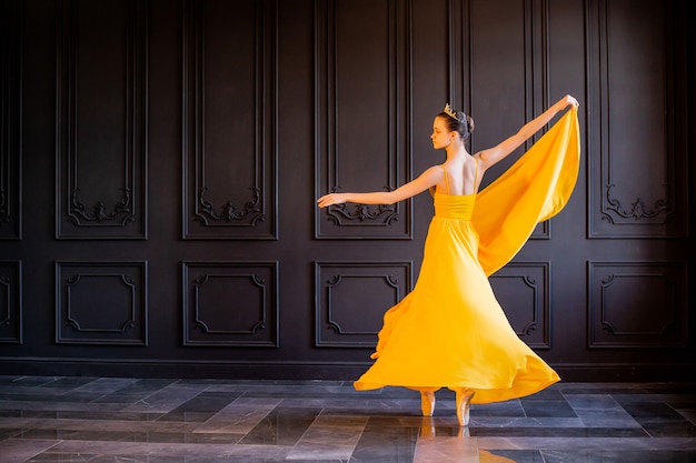 Une élégante ballerine en pointes danse avec un tissu jaune fluide sur fond gris foncé