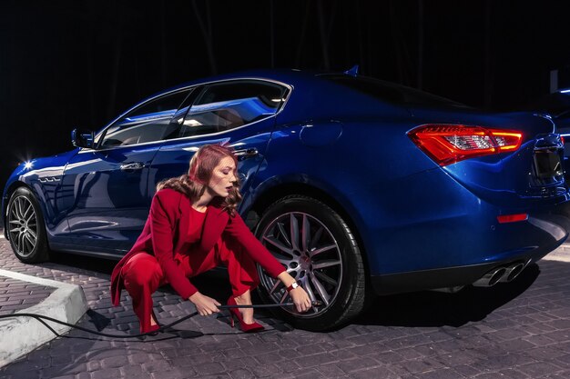 L'élégante belle femme remplissant l'air dans un pneu de voiture pour augmenter la pression du pneu de voiture.