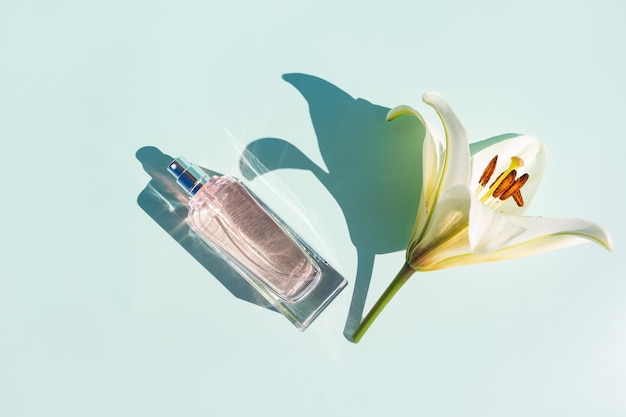 Une élégante bouteille de parfum ou de vaporisateur pour femme avec un parfum floral sur fond pastel avec une fleur de lys blanc une ombre ensoleillée de l'espace de copie