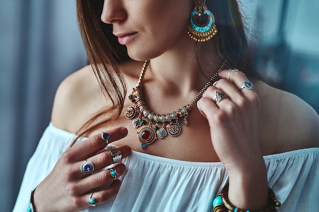 Photo Élégante femme boho brune portant un chemisier blanc avec de grandes boucles d'oreilles, un collier avec des anneaux en pierre et en argent. tenue bohème gitane hippie indienne à la mode avec des détails de bijoux d'imitation