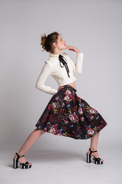 élégante jeune femme en jupe longue à motif floral noir, veste posant sur fond blanc