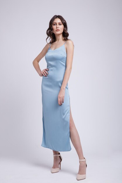 élégante jeune femme vêtue d'une jolie robe bleue, posant sur fond blanc. Silhouette mince, prise de vue en studio