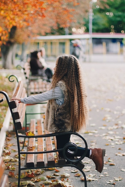 Photo Élégante petite fille de 4 à 5 ans portant des bottes, manteau de fourrure avec de très longs cheveux bouclés. vue de dos. automne saison d'automne