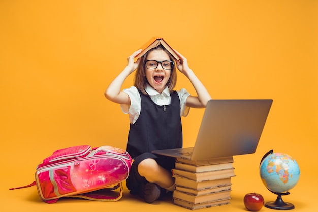 Un élève émotif est assis derrière une pile de livres et un ordinateur portable tient un livre sur le concept d'éducation des enfants en tête