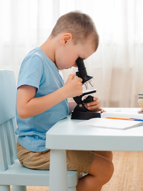 L'élève est assis à table et engagé dans du matériel éducatif. écolier regarde à travers un microscope.