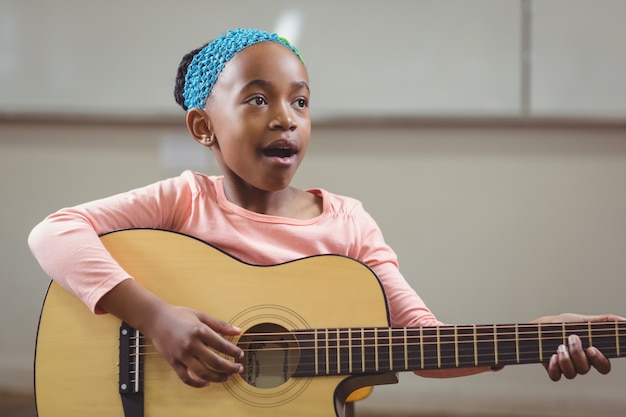 Élève mignon chantant et jouant de la guitare dans une salle de classe