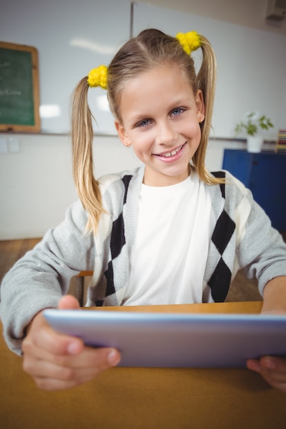 Élève souriant à l&#39;aide de tablette à son bureau dans une salle de classe
