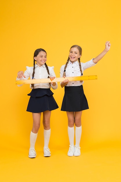 Des élèves confiants de petites filles heureuses étudient les mathématiques les élèves utilisent les disciplines de la tige de la règle jaune pour retourner à l'école Mathématiques et géométrie Enfants en uniforme mesurant l'amitié scolaire