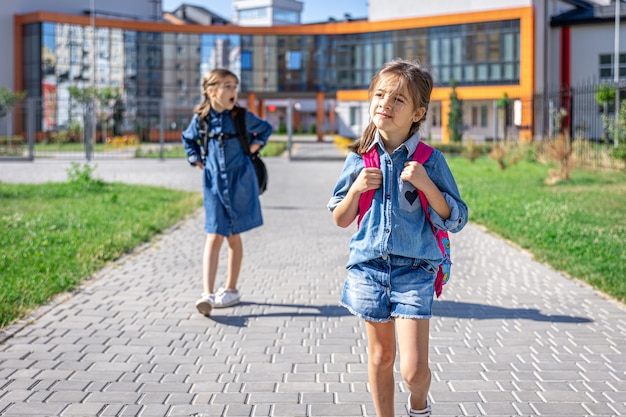 Elèves de l'école primaire. Filles avec des sacs à dos près du bâtiment à l'extérieur. Début des cours. Premier jour d'automne.