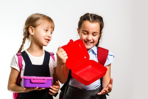 Elèves de l'école primaire avec des lunch-boxes à la main. Les filles avec des sacs à dos mangent des fruits. Début des cours. Premier jour d'automne.