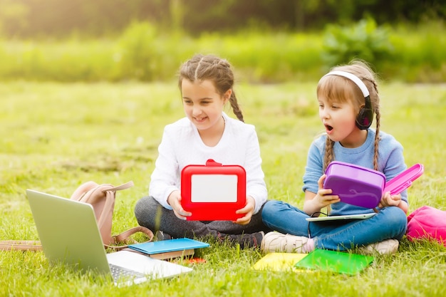 Elèves de l'école primaire avec des lunch-boxes à la main. Des filles avec des sacs à dos mangent sur la pelouse. Début des cours. Premier jour d'automne.