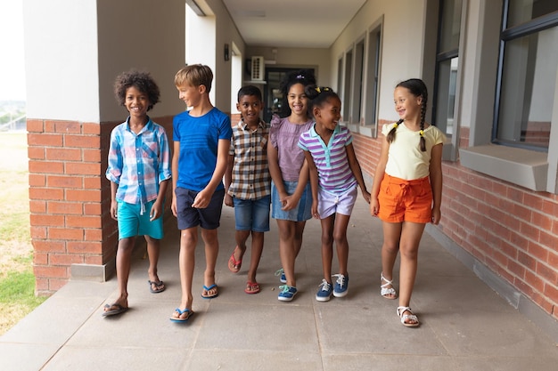 Des élèves d'école primaire multiraciaux souriants marchant dans le couloir de l'école.