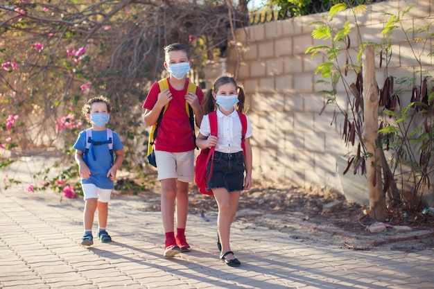 Les élèves avec des masques médicaux sur le visage et des sacs à dos en plein air. Éducation pendant la période des coronavirus. Les enfants et la santé. Retour à l'école.