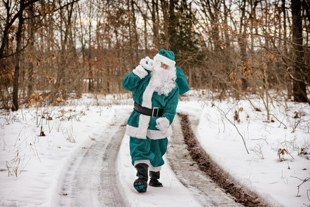 Elfe De Noël En Robe De Costume Vert Apporte La Marche à Travers La Forêt D'hiver Transportant Des Cadeaux De Noël Du Nouvel An Et En Détournant Les Yeux