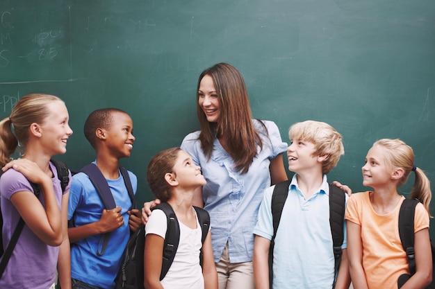 Elle crée une classe si heureuse Une jolie jeune enseignante debout avec sa classe au tableau noir et souriant